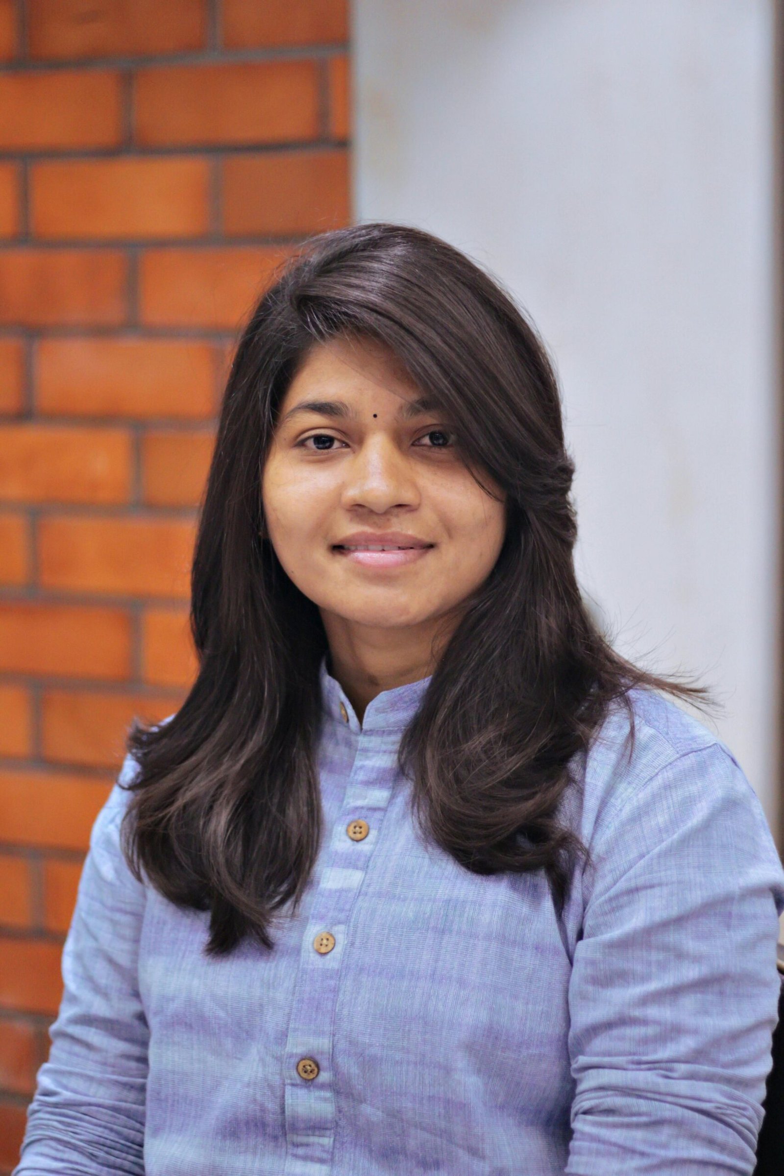 A confident woman with long black hair smiling in a portrait setting indoors.