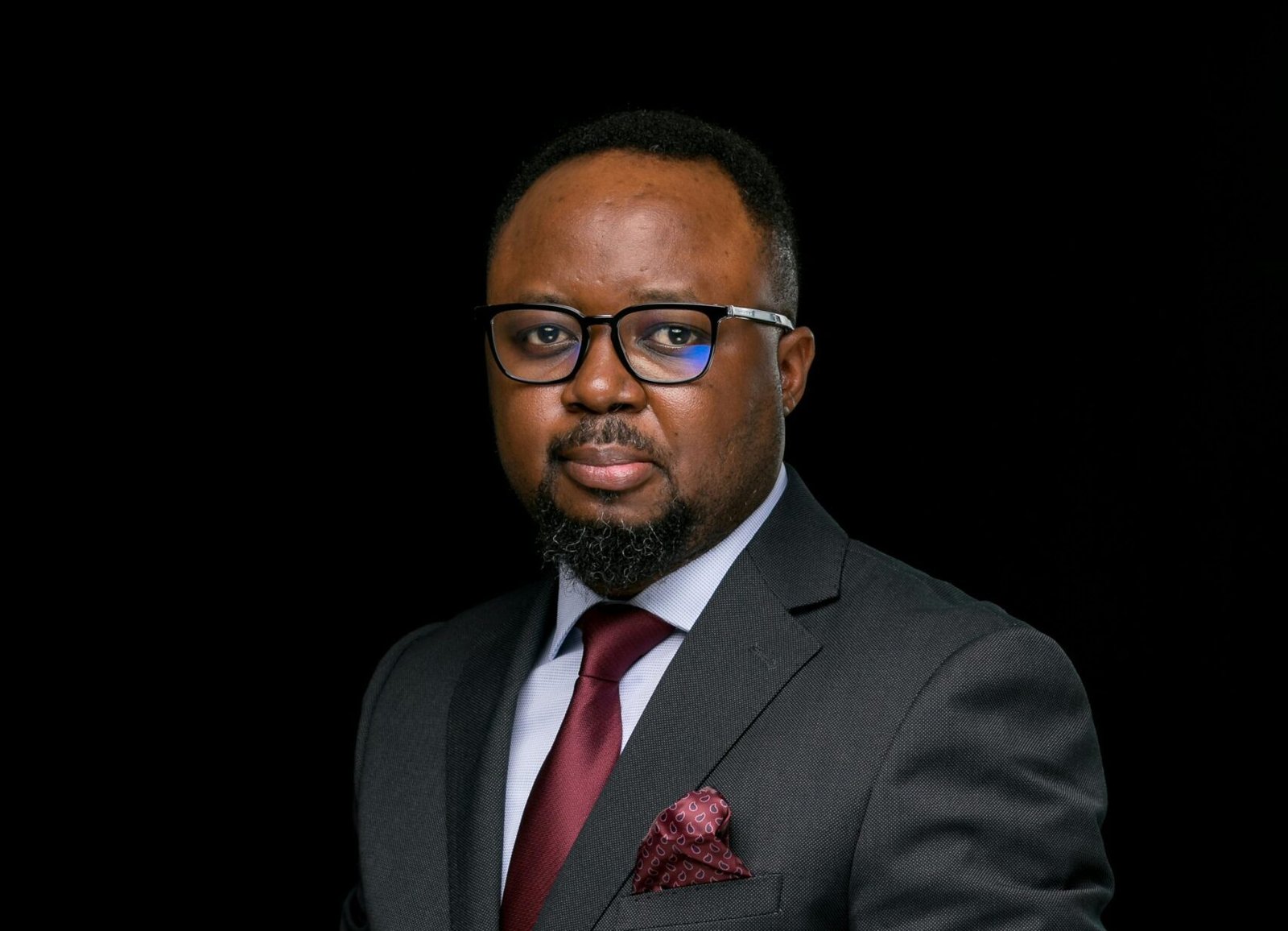 Elegant portrait of a businessman with beard and glasses, wearing a suit against a black background.